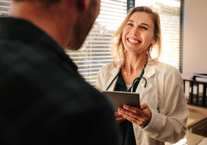 a medical professional holds a clipboard and smiles at her patient while explaining to them about how medication-assisted treatment can help their recovery