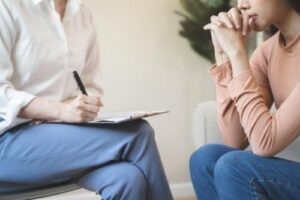 a patient sits with their hands to their mouth while their therapist sits across taking notes in the patients bipolar disorder treatment