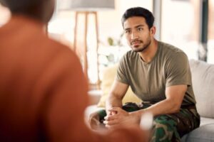 man in a military uniform sits and looks at his therapist in his veterans program